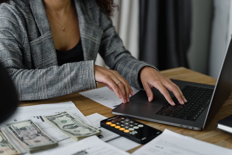 A woman using her laptop with money and telephone on the side.